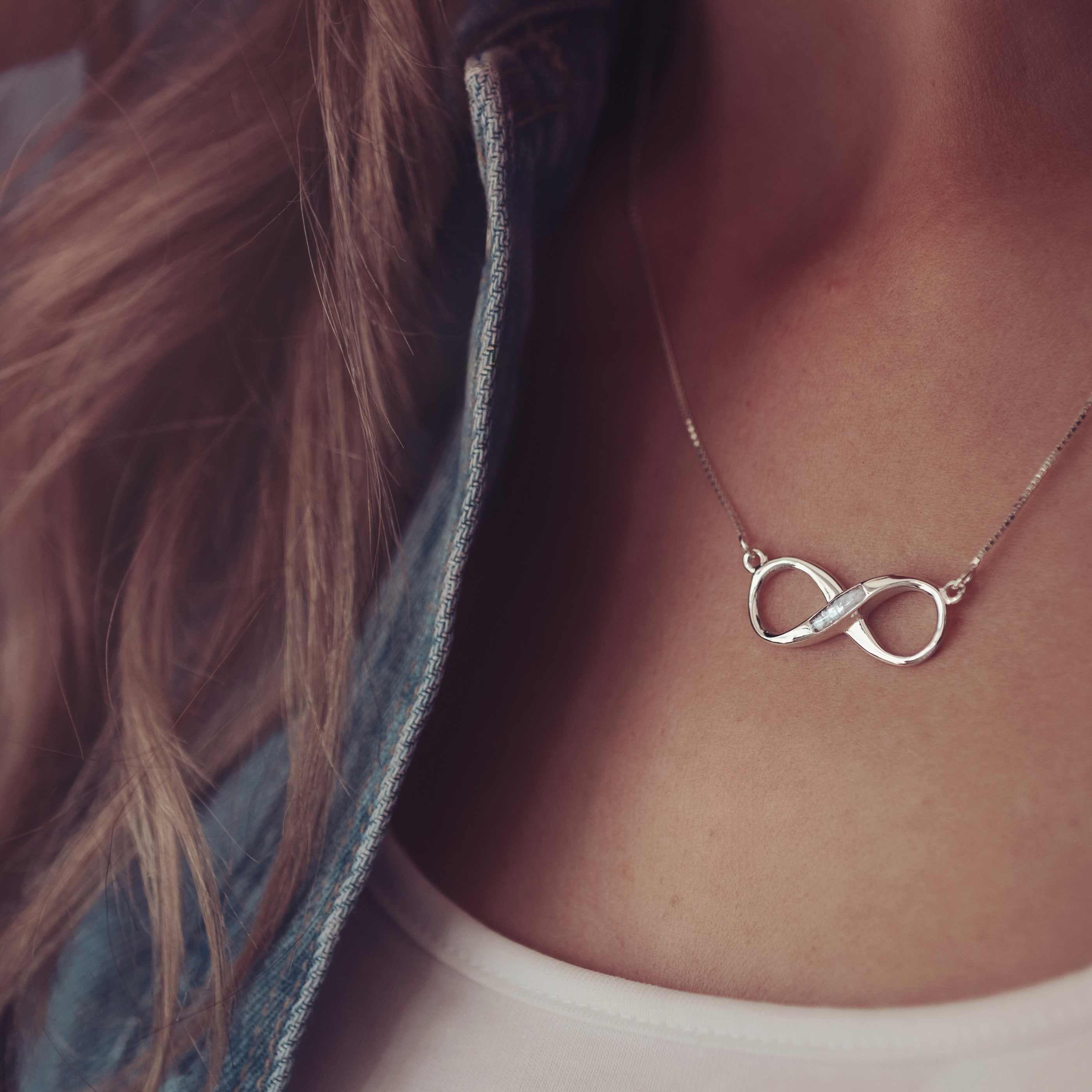 A silver infinity shaped necklace with the middle filled in with cremation ashes modelled on a lady.