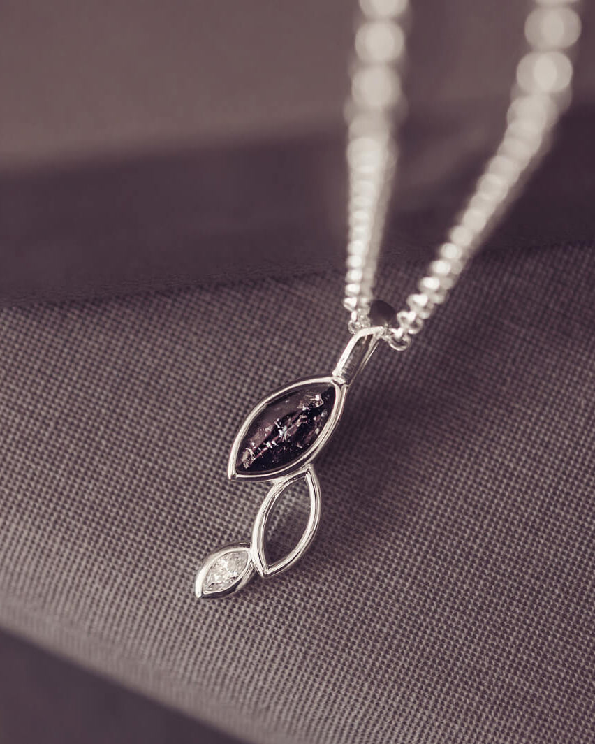 sterling silver necklace featuring gem stone, cremation ashes, black crystal and resin hung over a grey box