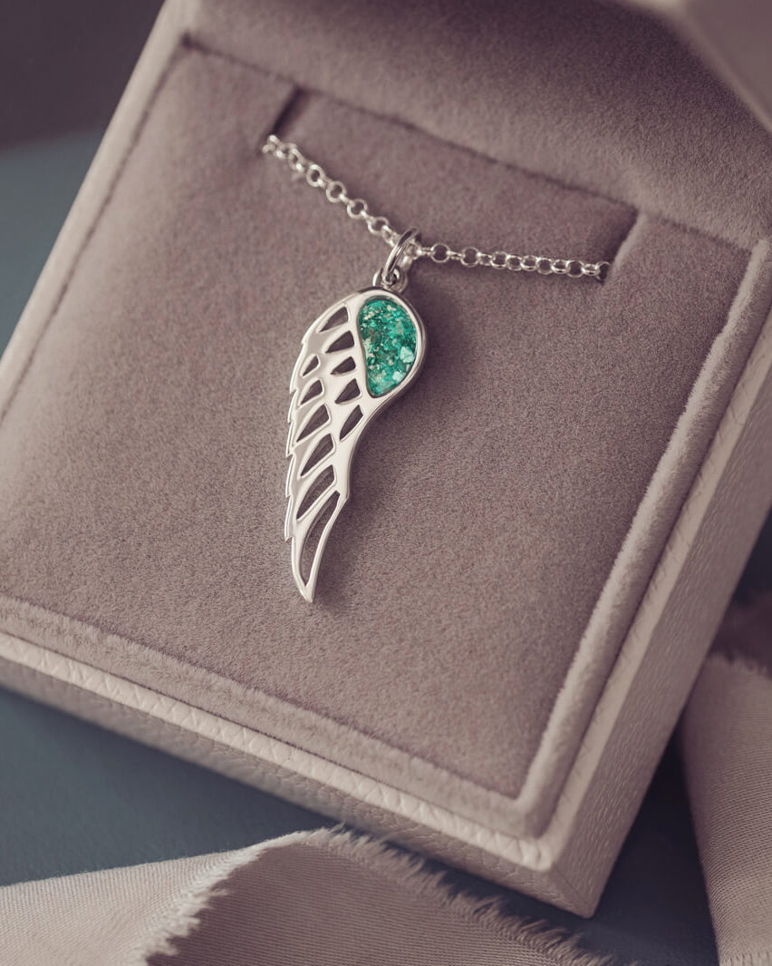Silver Angel Wing Necklace with green floating crystals which hold cremation ashes. Shown on a dark background