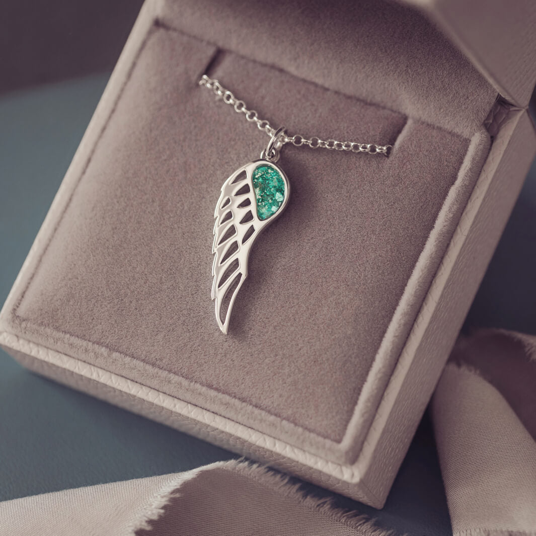 Silver Angel Wing Necklace with green floating crystals which hold cremation ashes. Shown on a dark background