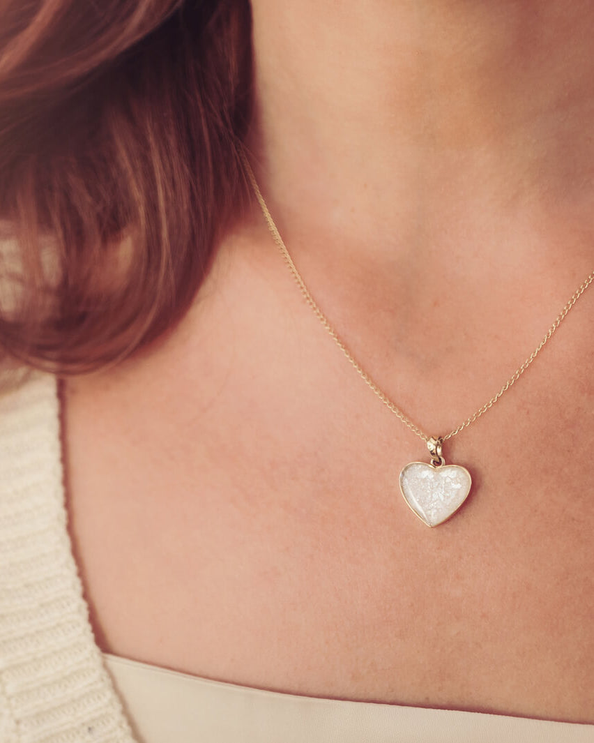 gold heart necklace filled with clear crystals, resin and cremation ashes, worn on a gold chain around a ladies neck