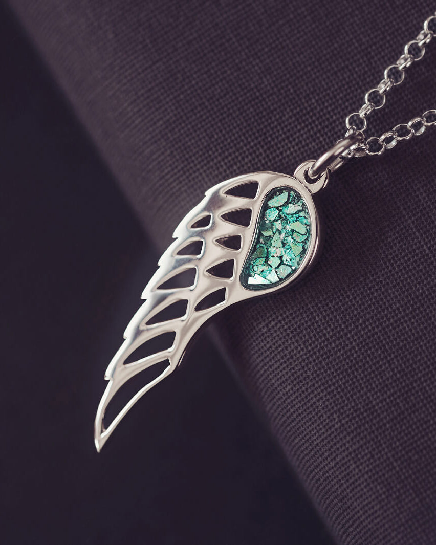 Silver Angel Wing Necklace with green floating crystals which hold cremation ashes. Shown on a dark background