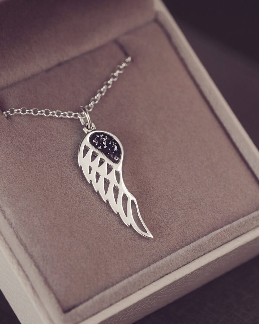 Silver Angel Wing Necklace with black floating crystals which hold cremation ashes. Shown on in a grey jewellery box