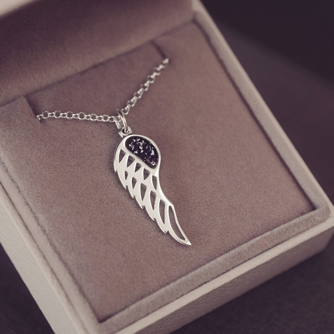 Silver Angel Wing Necklace with black floating crystals which hold cremation ashes. Shown on in a grey jewellery box