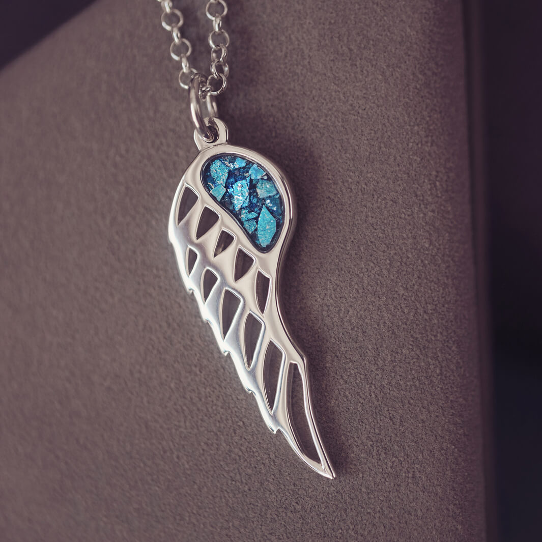 Silver Angel Wing Necklace with blue floating crystals which hold cremation ashes. Shown on a dark background