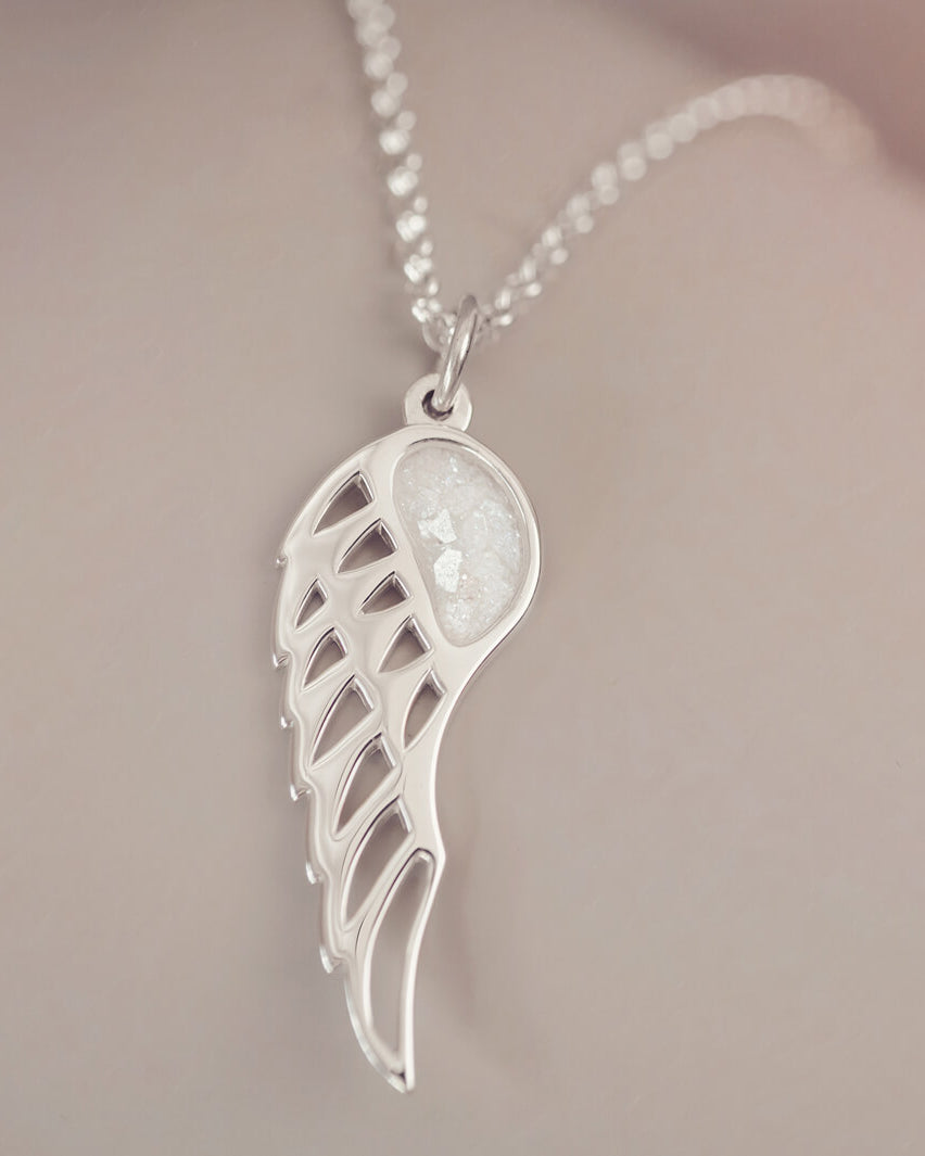 Silver Angel Wing Necklace with clear floating crystals which hold cremation ashes. Shown on a light grey background