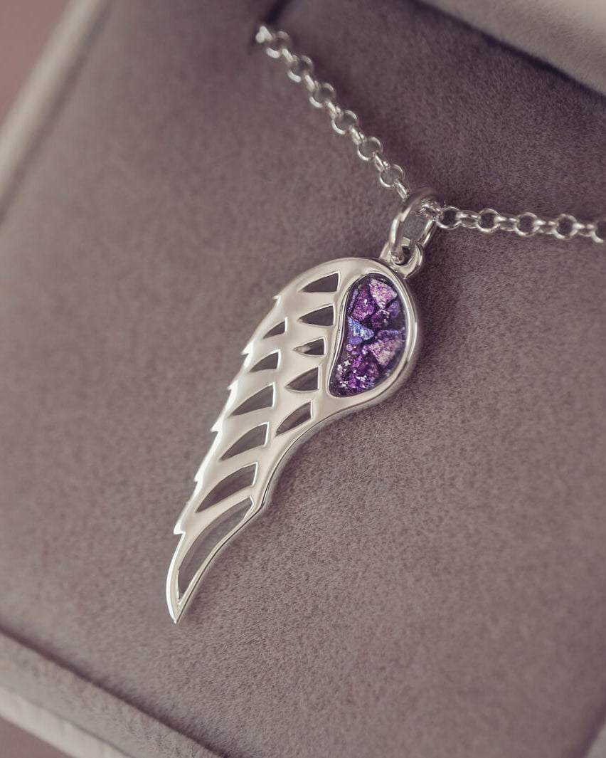 Silver Angel Wing Necklace with purple floating crystals which hold cremation ashes. Shown in a grey jewellery box