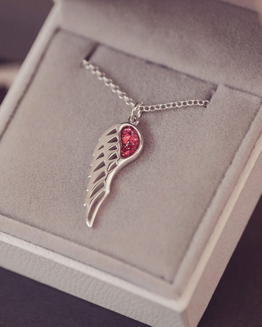 Silver Angel Wing Necklace with red floating crystals, which holds cremation ashes. Shown in a grey jewellery box