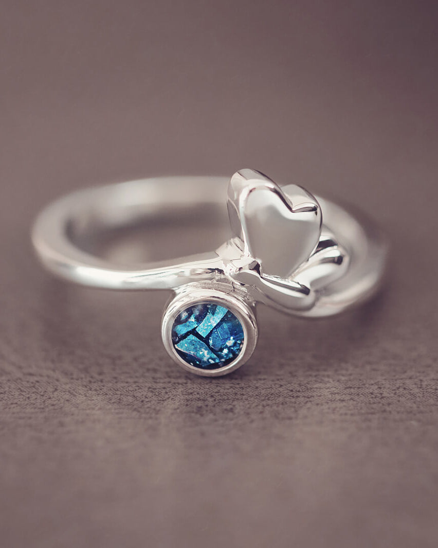 Silver butterfly ring with blue floating crystals and cremation ashes on a grey background