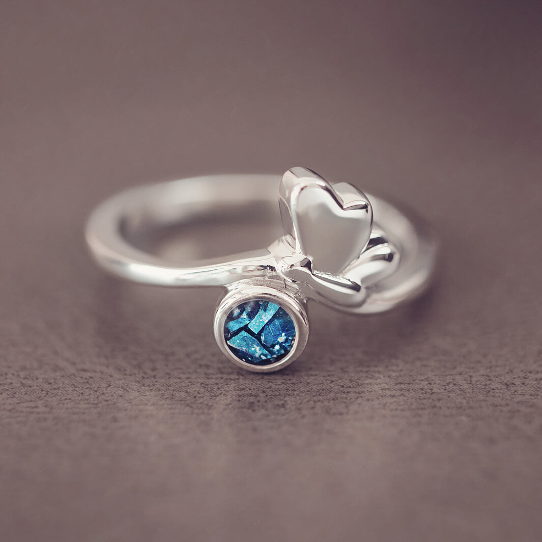 Silver butterfly ring with blue floating crystals and cremation ashes on a grey background