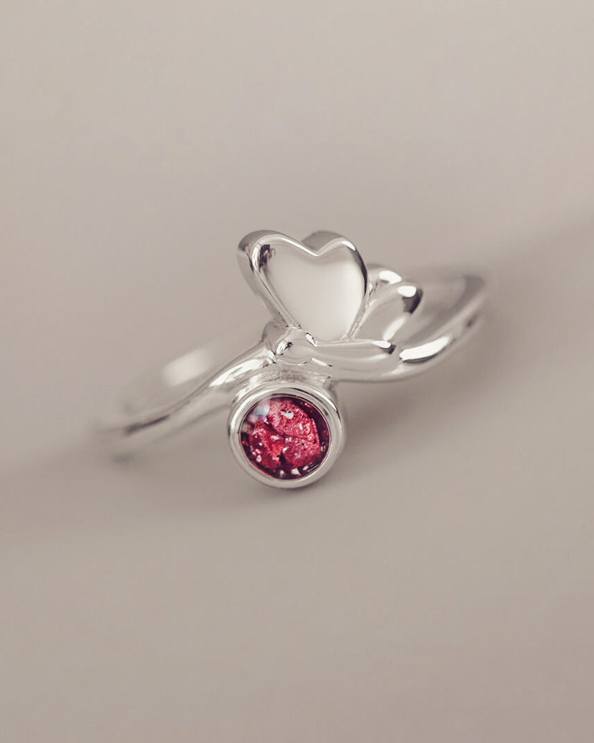 Silver Butterfly Ring with red crystals and cremation ashes on a grey background