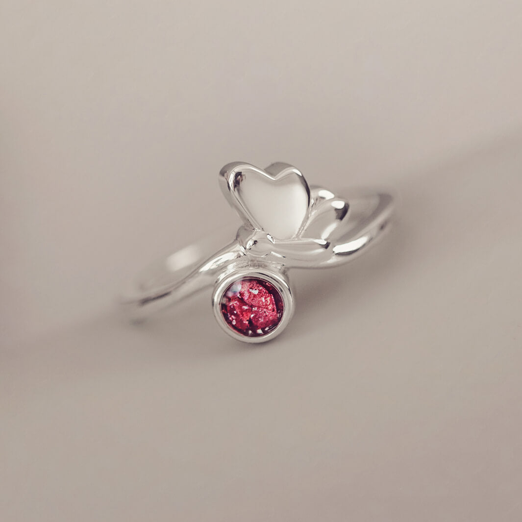 Silver Butterfly Ring with red crystals and cremation ashes on a grey background