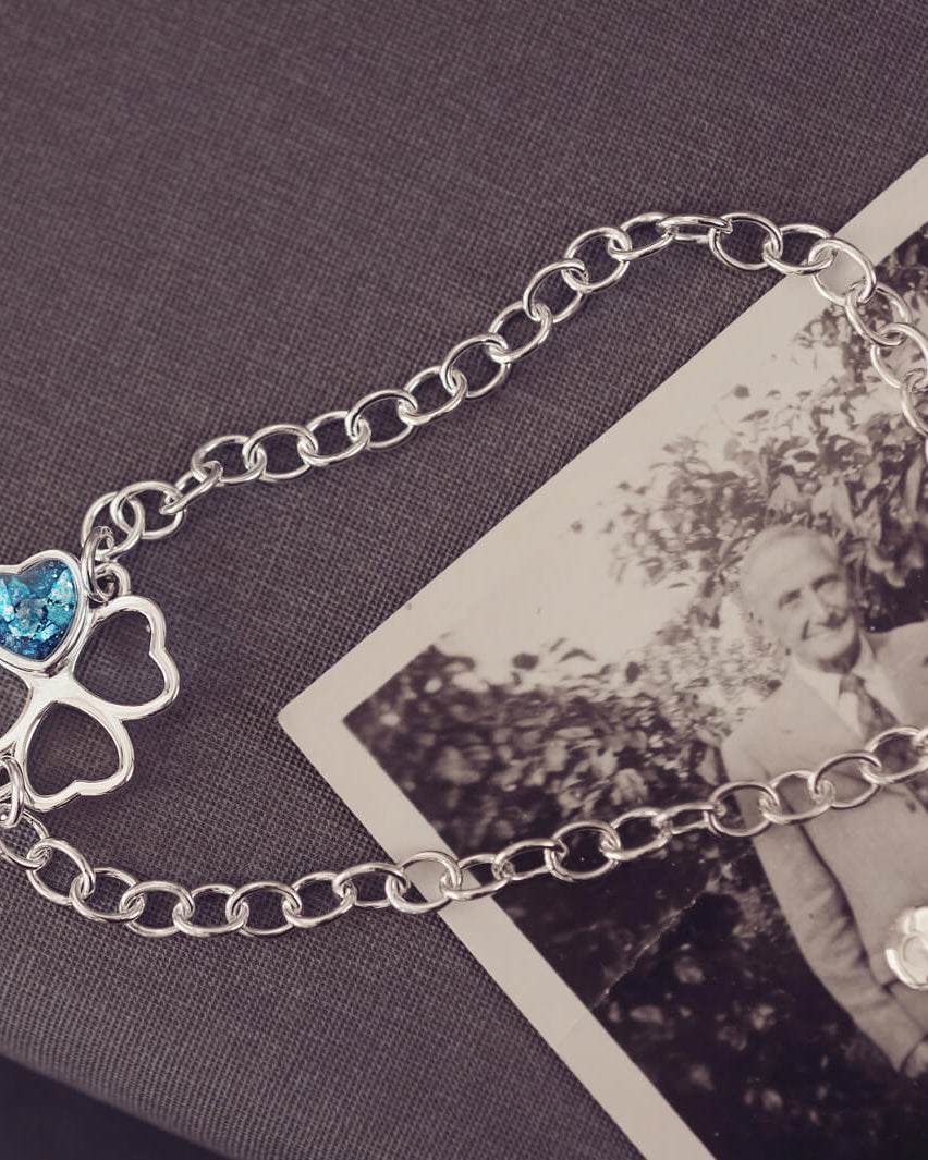 sterling silver chain bracelet with clover shaped charm holding blue crystal and cremation ashes sat on top of a black and white photo