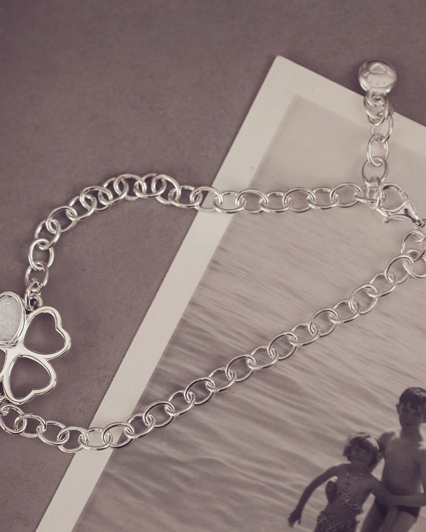 sterling silver chain bracelet with clover shaped charm holding clear crystal and cremation ashes sat on top of a black and white photo