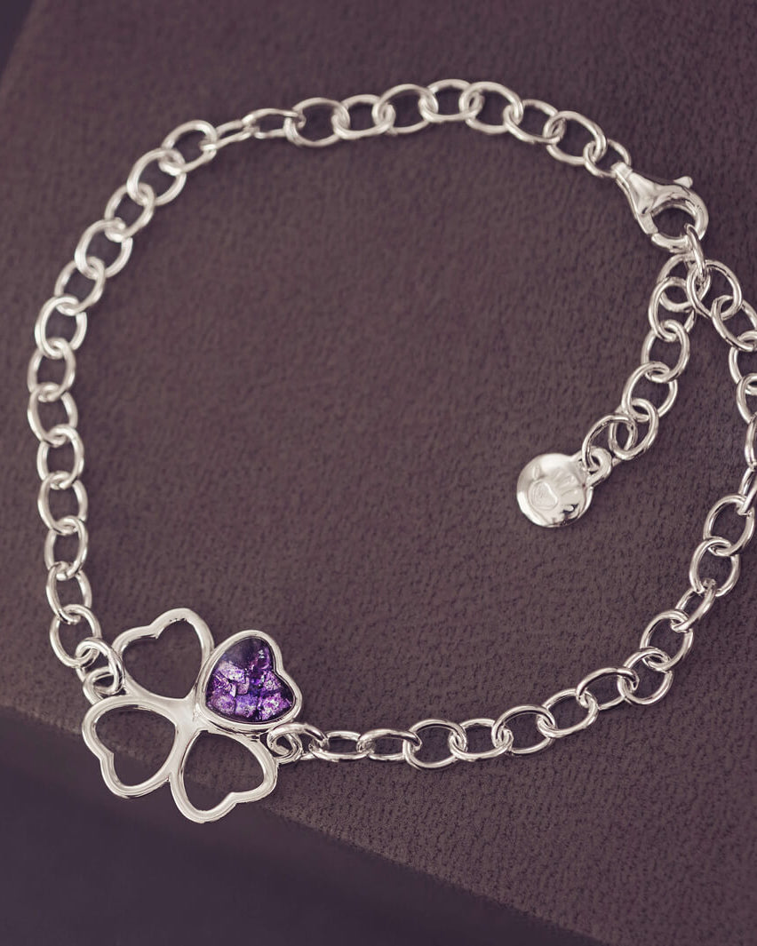 sterling silver chain bracelet with clover shaped charm holding purple crystal and cremation ashes on a black/purple background