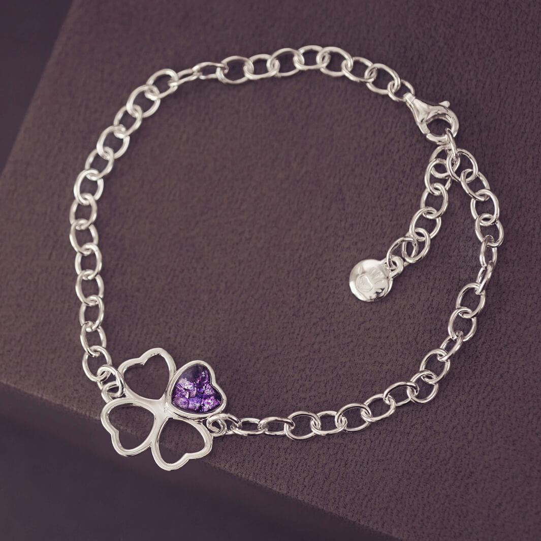 sterling silver chain bracelet with clover shaped charm holding purple crystal and cremation ashes on a black/purple background