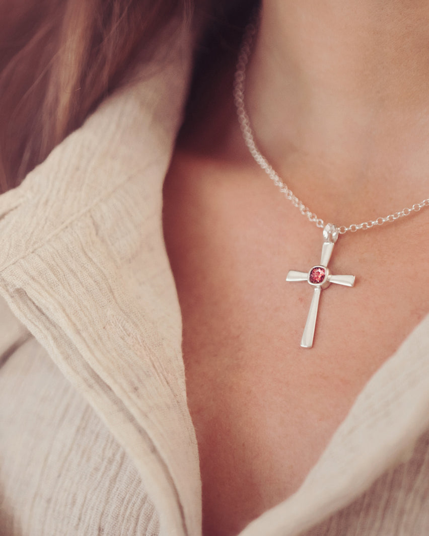 silver cross necklace with a section of resin and red crystals, holding memorial ashes, worn around a ladies neck