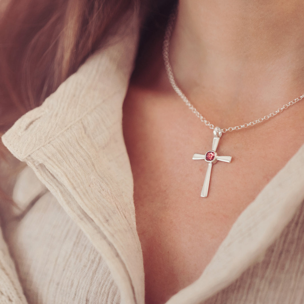 silver cross necklace with a section of resin and red crystals, holding memorial ashes, worn around a ladies neck