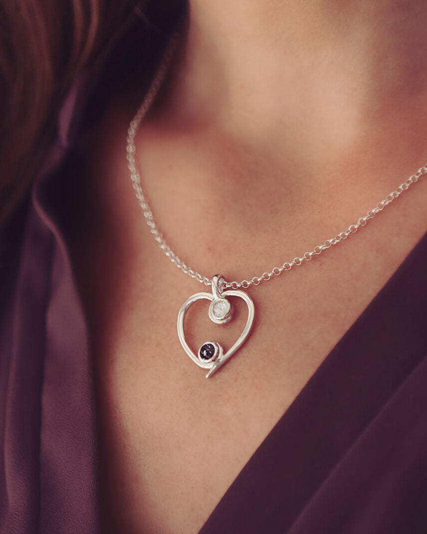 A silver heart-shaped pendant necklace featuring two sparkling resin stones, holding cremation ashes, worn on a ladies neck