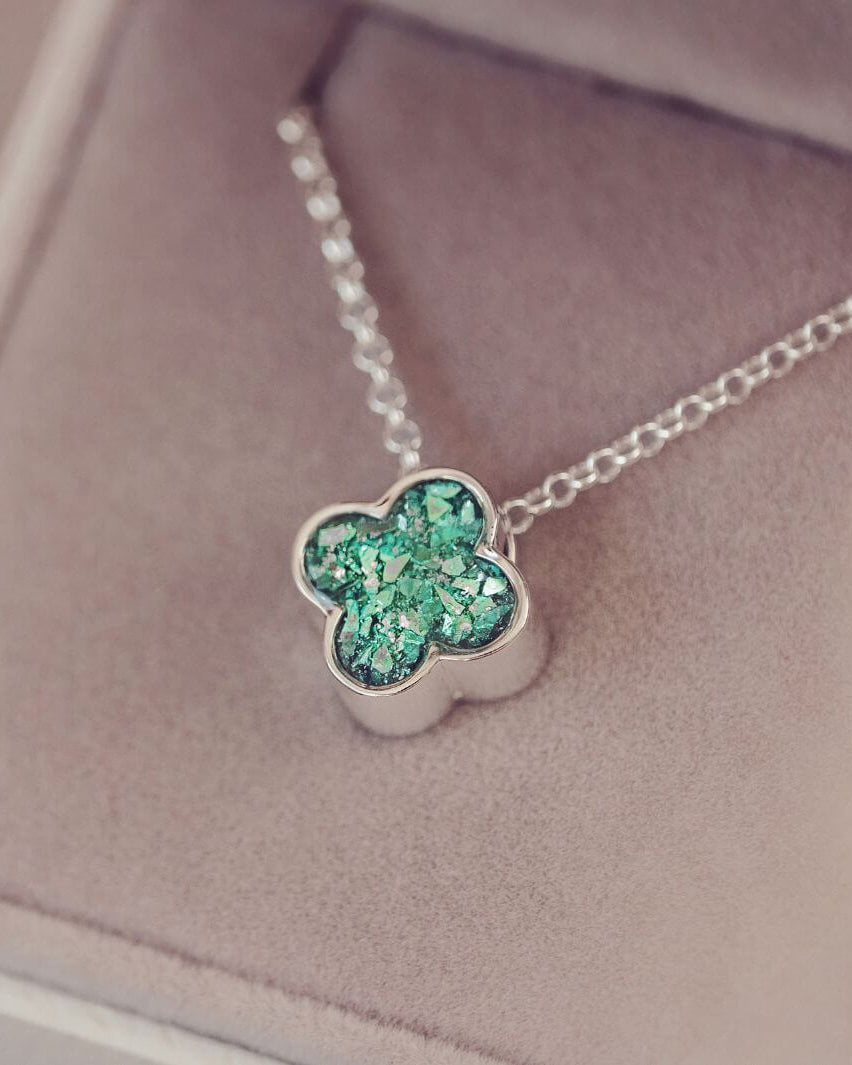 Silver necklace with a green clover-shaped pendant on a soft pink background