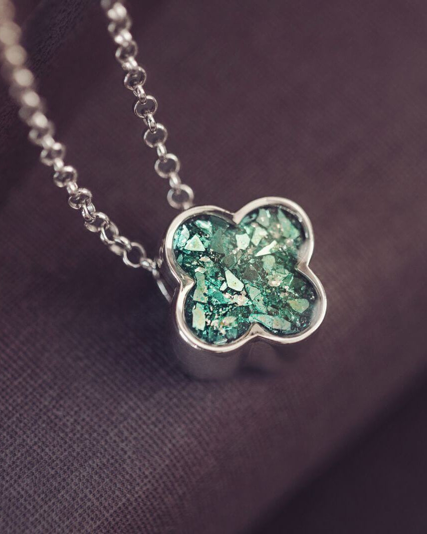 Silver necklace with a green clover-shaped pendant on a soft pink background