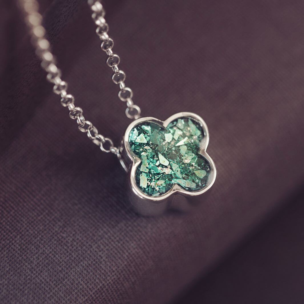 Silver necklace with a green clover-shaped pendant on a soft pink background