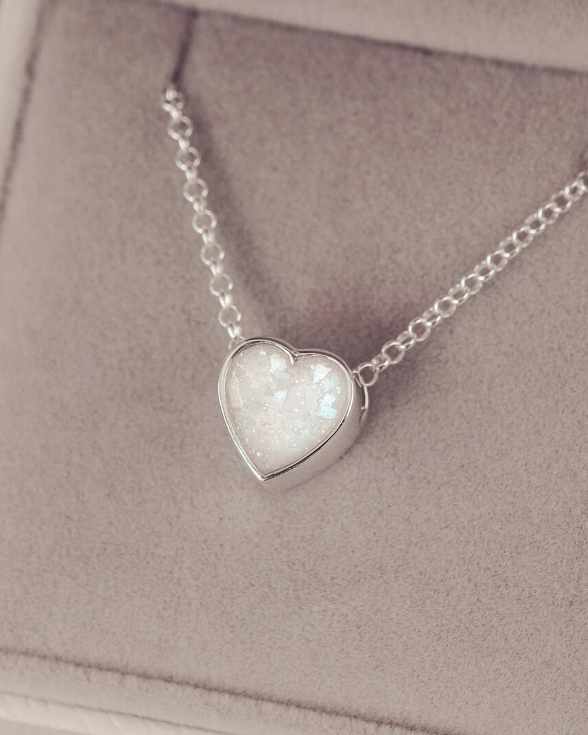 White or clear heart pendant, filled with crystals, glitter and memorial ashes, on a silver chain.