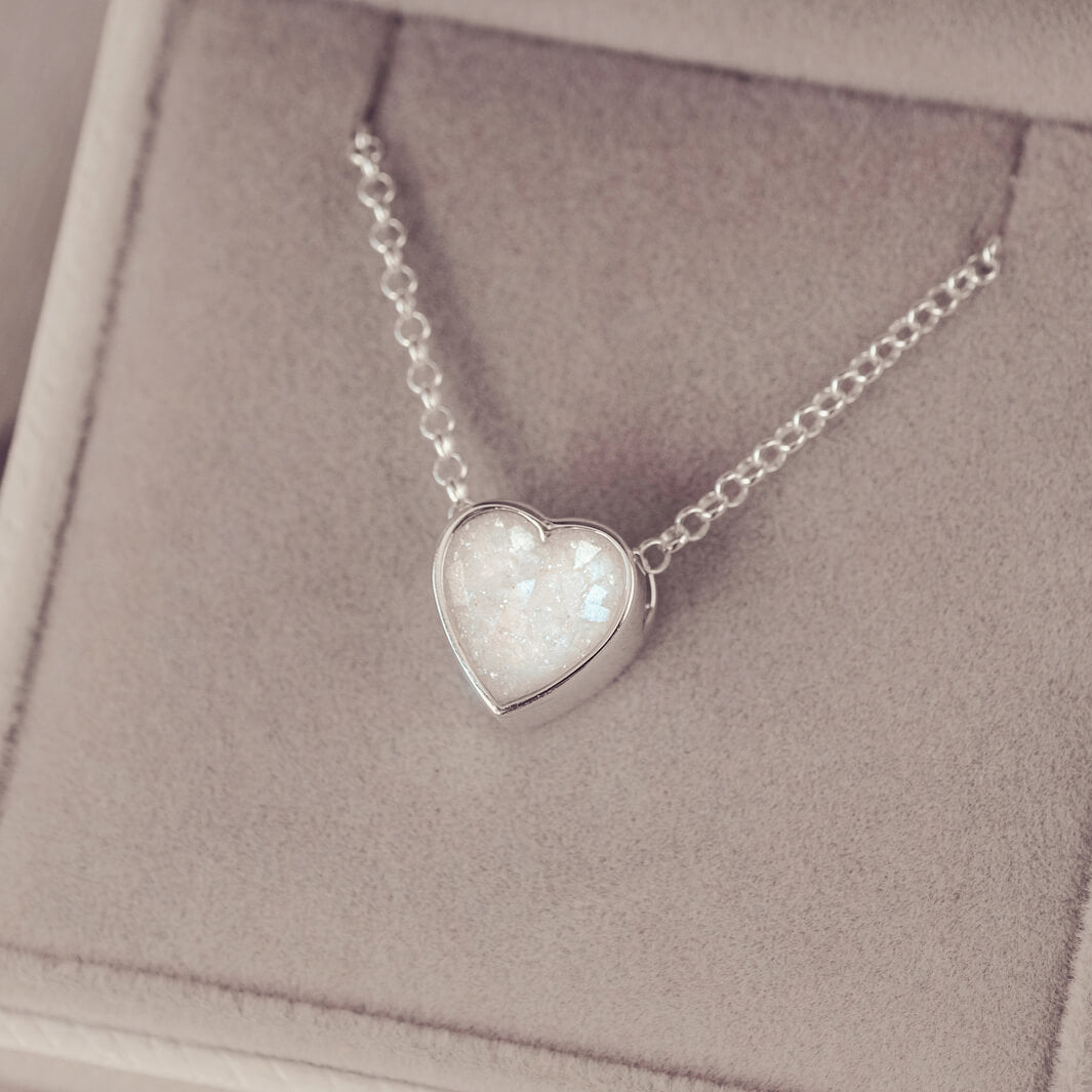 White or clear heart pendant, filled with crystals, glitter and memorial ashes, on a silver chain.