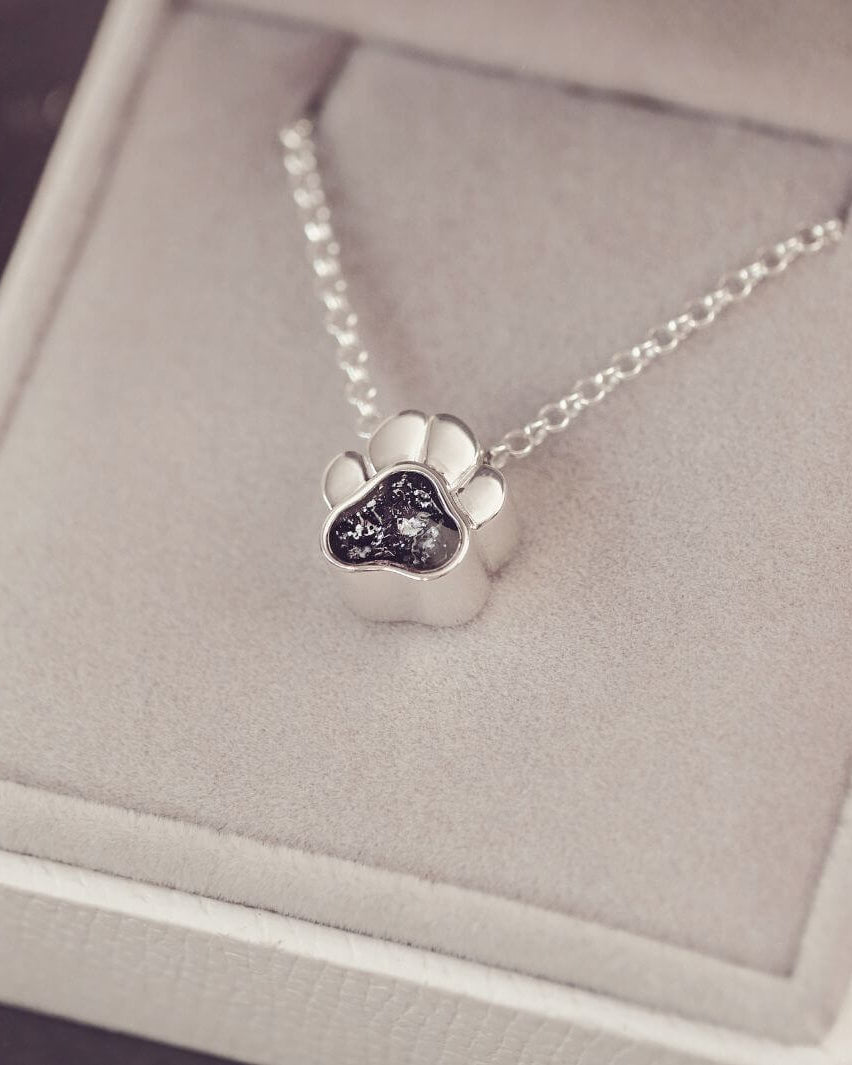 Silver paw print necklace on a gray jewellery box
