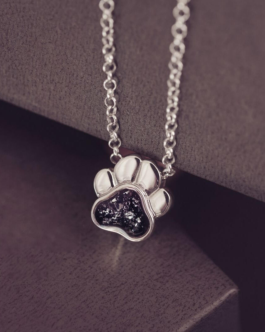Silver paw print necklace with dark gemstone on a dark surface