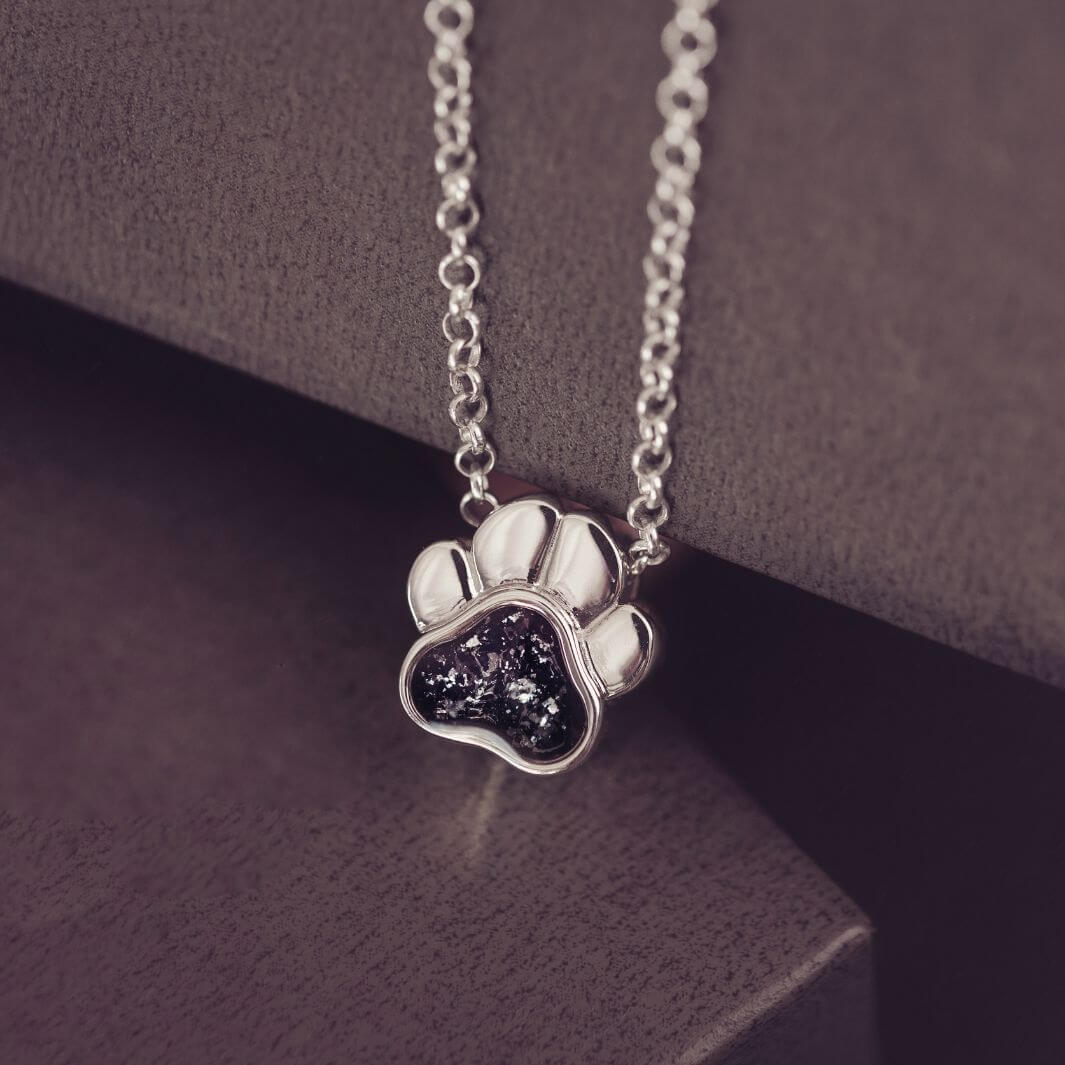 Silver paw print necklace with dark gemstone on a dark surface