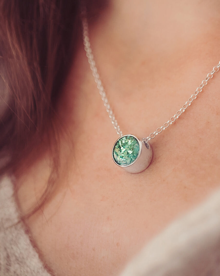 Sterling Silver Floating Round Pendant, filled with cremation ashes and green crystal, on a chain on a ladies neck
