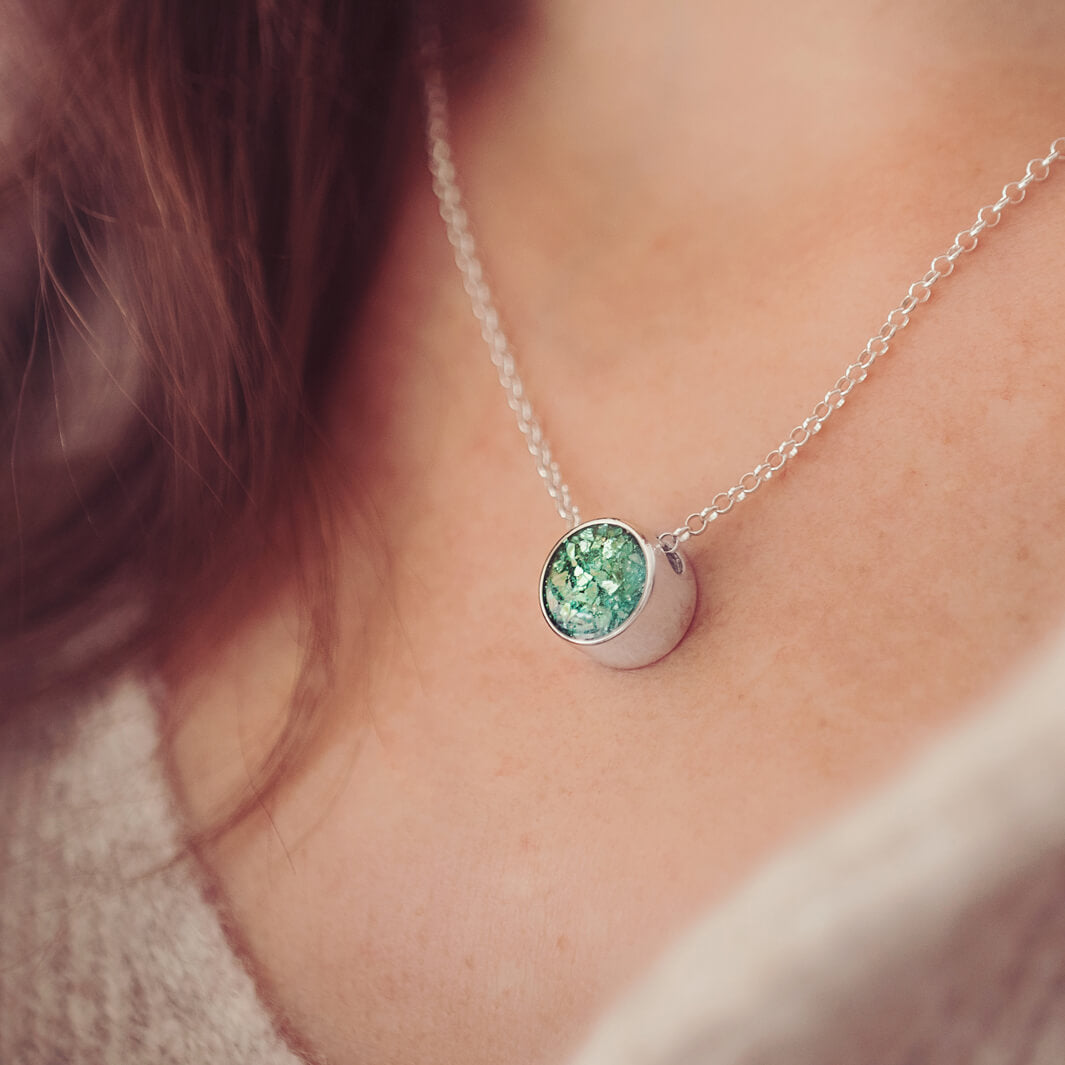 Sterling Silver Floating Round Pendant, filled with cremation ashes and green crystal, on a chain on a ladies neck