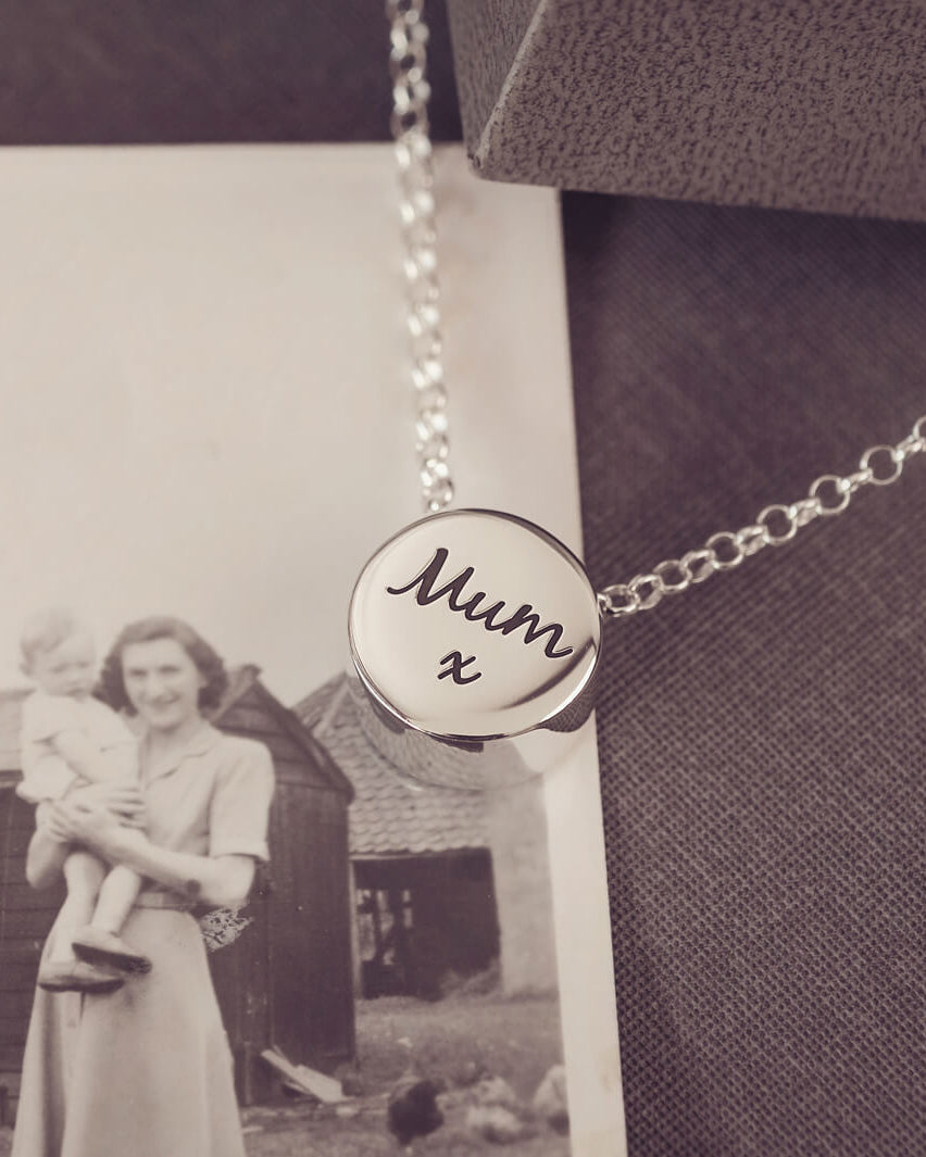 Round silver charm on silver chain, with the message 'Mum x' engraved on the reverse