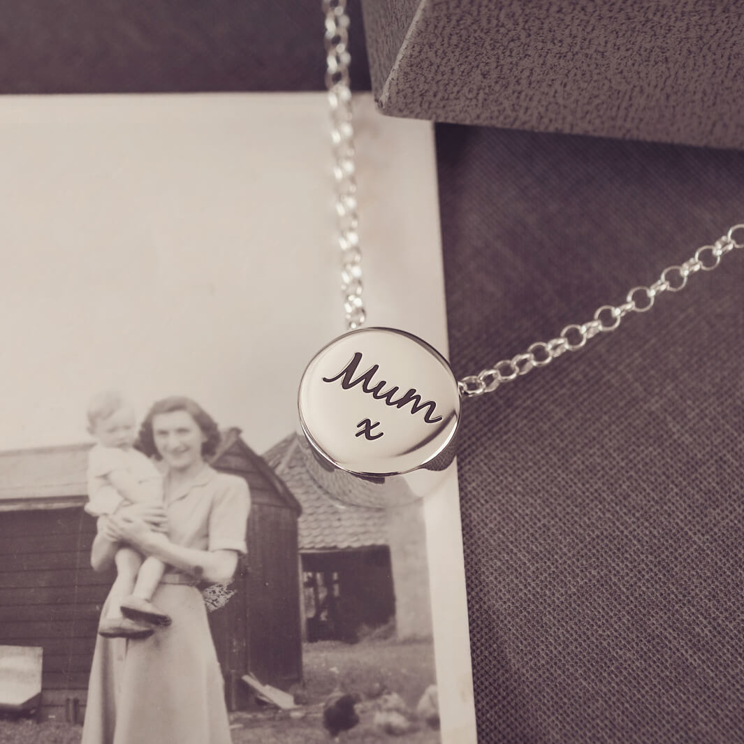Round silver charm on silver chain, with the message 'Mum x' engraved on the reverse