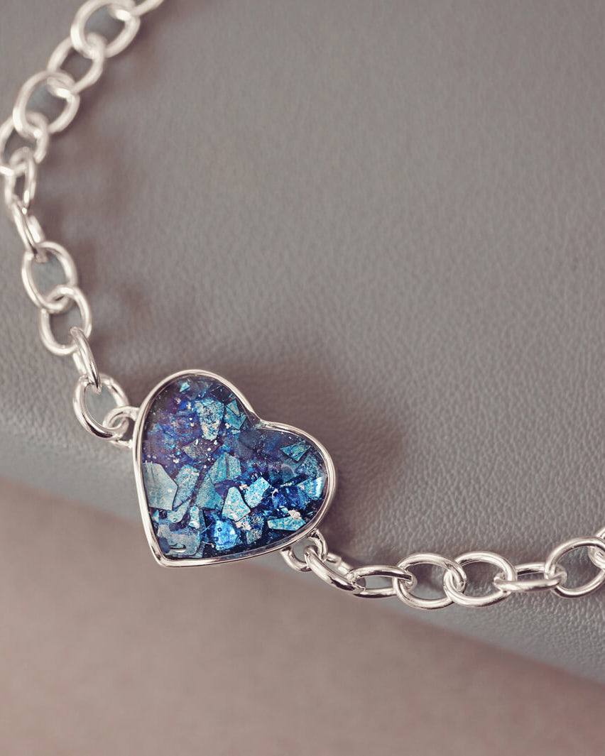 silver bracelet & heart charm, holding blue crystal, resin & cremation ashes. laying on a black grey ground