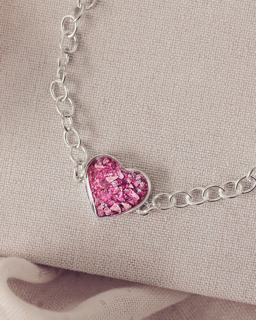 silver bracelet & heart charm, holding pink crystal, resin & cremation ashes. laying on a beige back ground