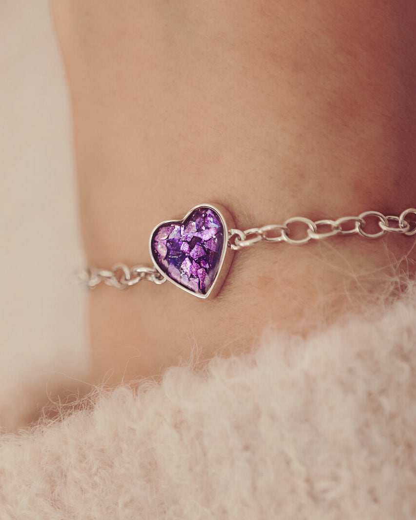 silver bracelet & heart charm, holding purple crystal, resin & cremation ashes. Worn on a ladies wrist.
