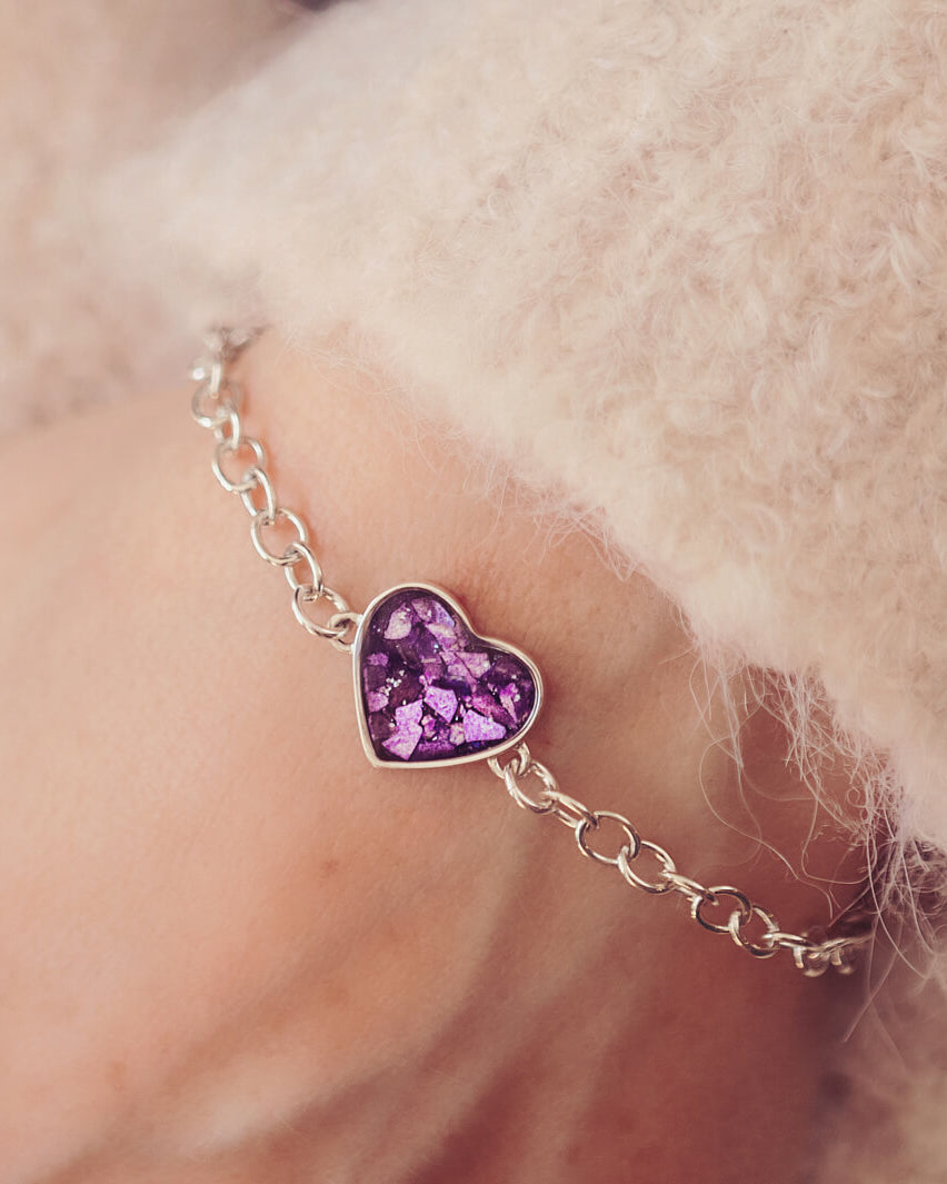 silver bracelet & heart charm, holding purple crystal, resin & cremation ashes. Worn on a ladies wrist.