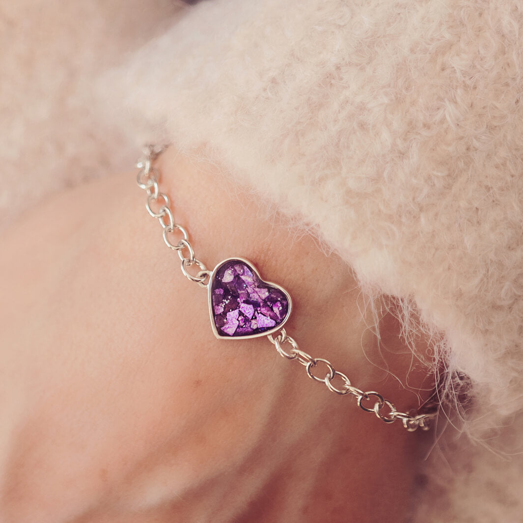 silver bracelet & heart charm, holding purple crystal, resin & cremation ashes. Worn on a ladies wrist.