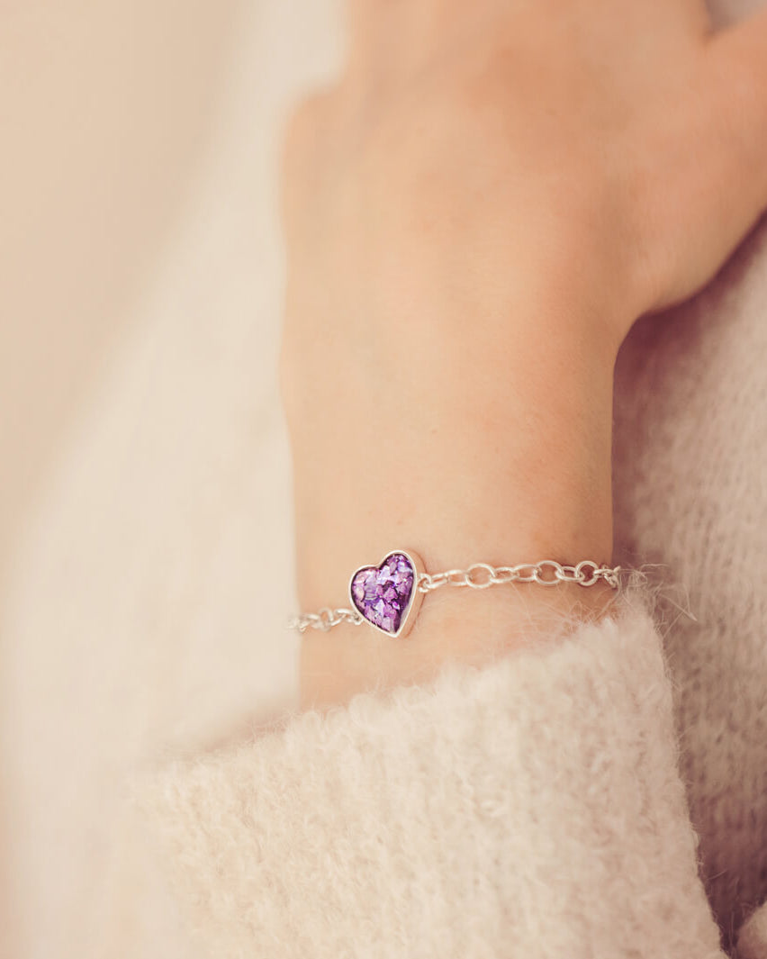 silver bracelet & heart charm, holding purple crystal, resin & cremation ashes. Worn on a ladies wrist.