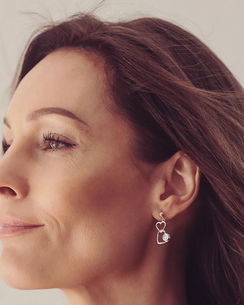 Silver Heart Dangle Earrings, holding cremation ashes, with clear crystals. Worn in a ladies ear.