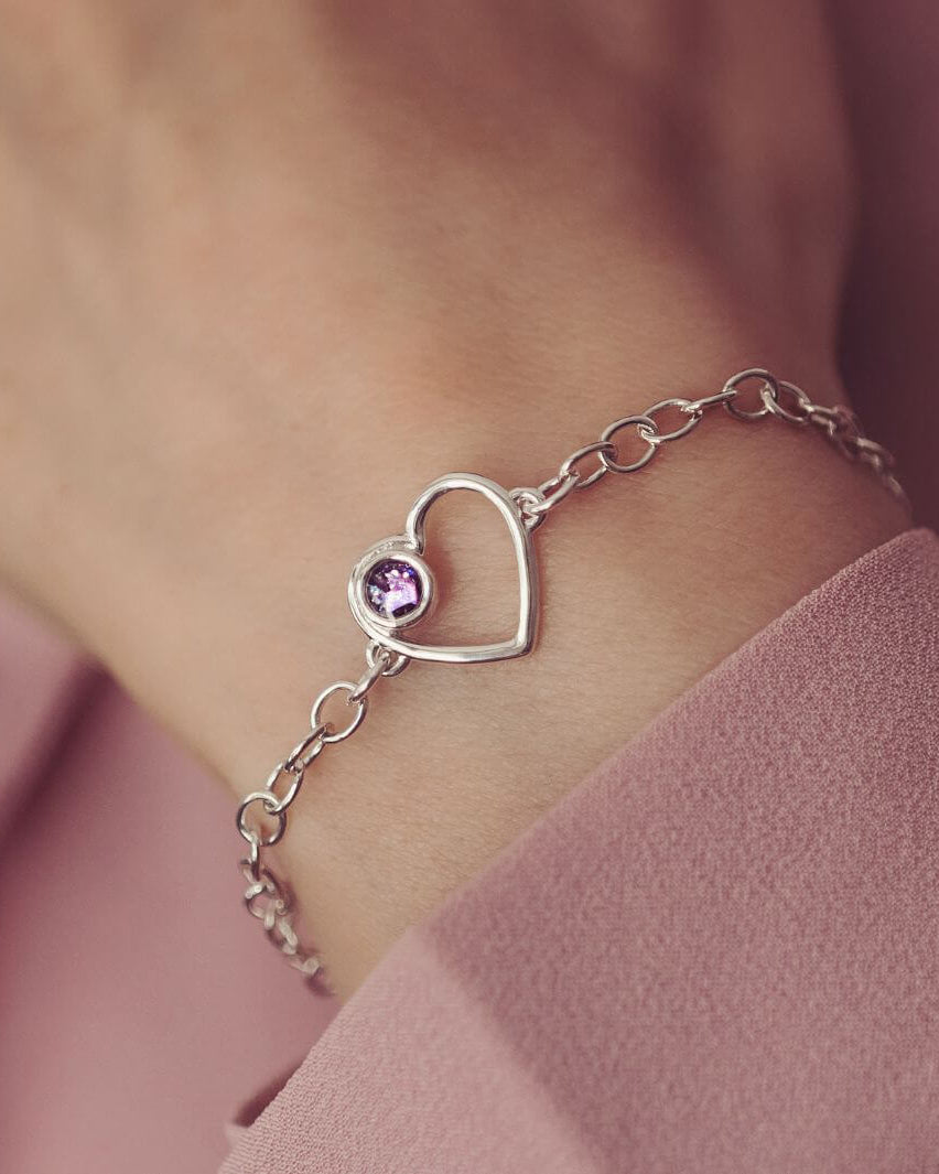 Silver bracelet with a purple heart cremation ashes charm on a wrist against a pink background