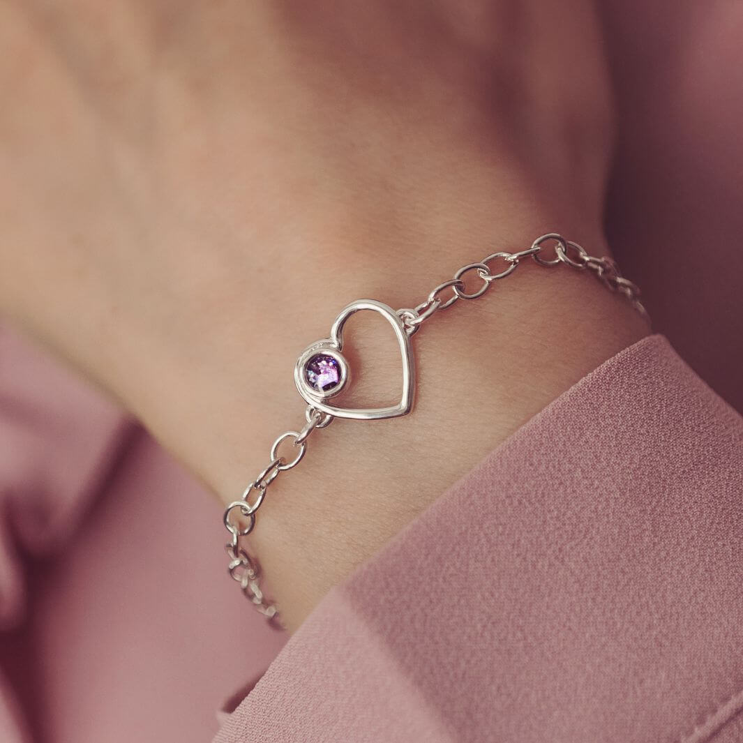 Silver bracelet with a purple heart cremation ashes charm on a wrist against a pink background
