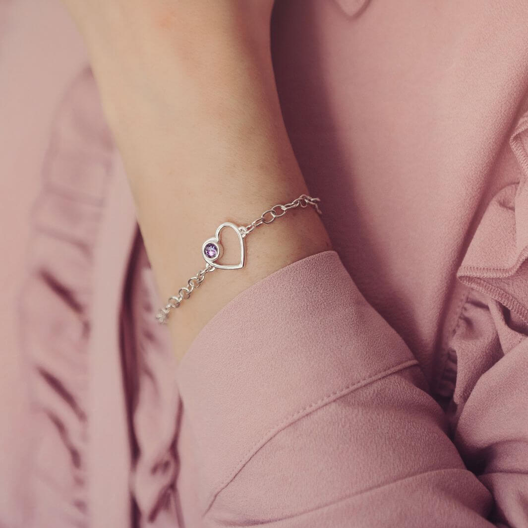Silver bracelet with a purple heart cremation ashes charm on a wrist against a pink background