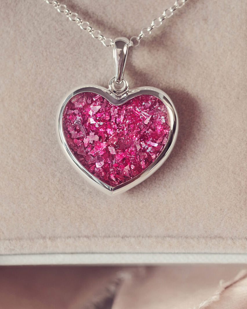 A sterling silver large heart pendant, hanging on a sterling silver belcher chain. The centre of the heart is filled with pink crystal and ashes.