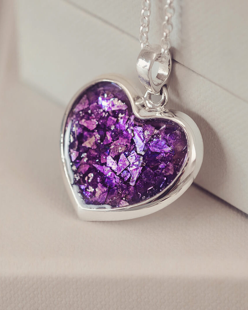 Sterling silver Large Heart necklace with a central section filled with memorial ashes and purple crushed crystals, displayed on a beige background.