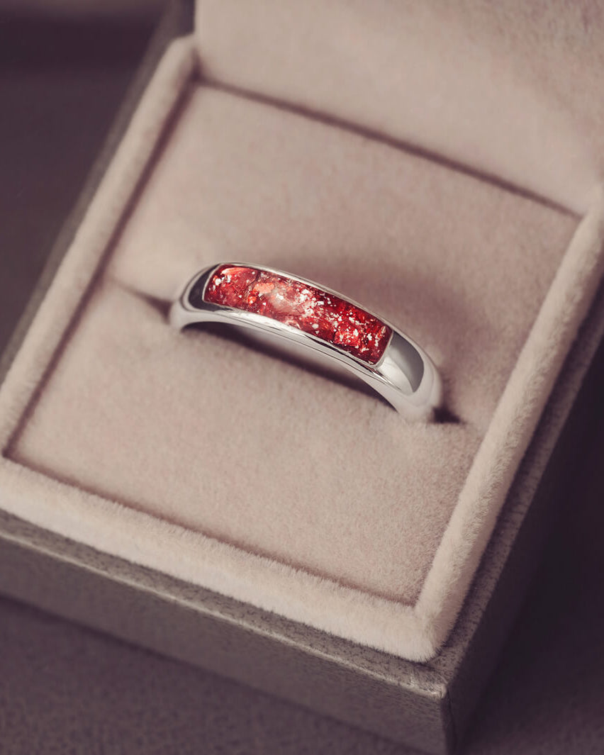 Sterling silver Mens Band Ring with a central section filled with memorial ashes and red crushed crystals, displayed in a grey jewellery box
