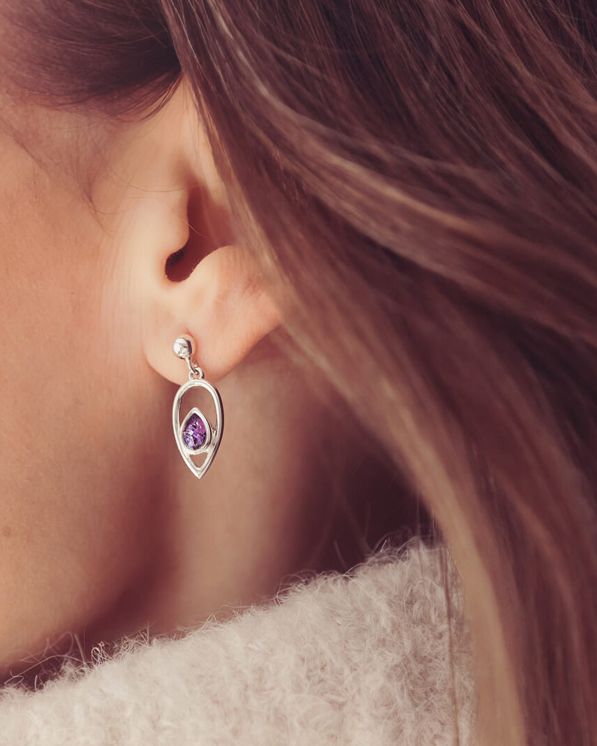 Cremation Ashes Peardrop Dangle Earrings filled with purple crystal and ashes, worn in a ladies ear