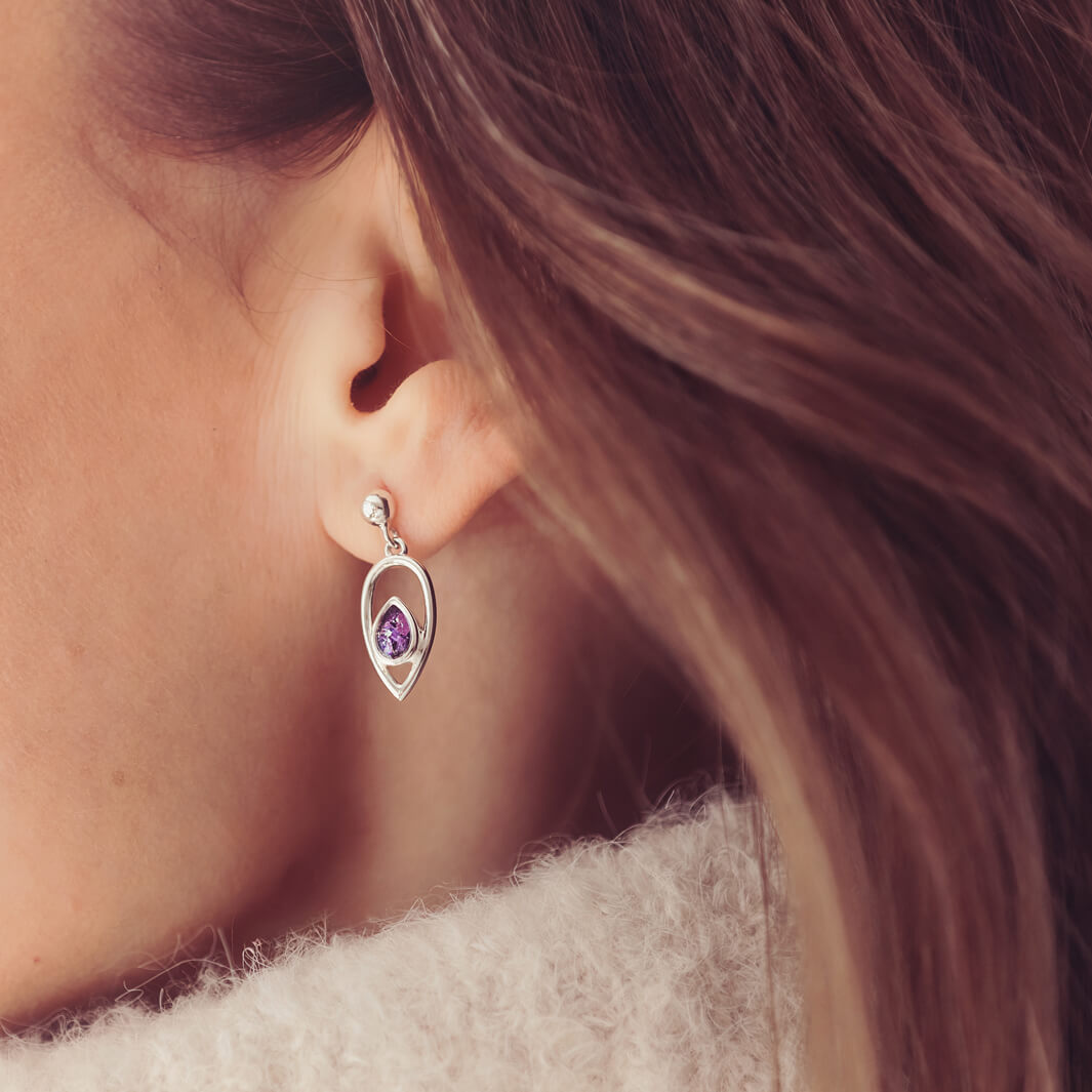 Cremation Ashes Peardrop Dangle Earrings filled with purple crystal and ashes, worn in a ladies ear